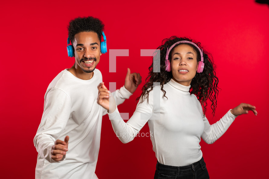 Young african american couple dancing with headphones isolated on red background studio. Party, happiness, music concept