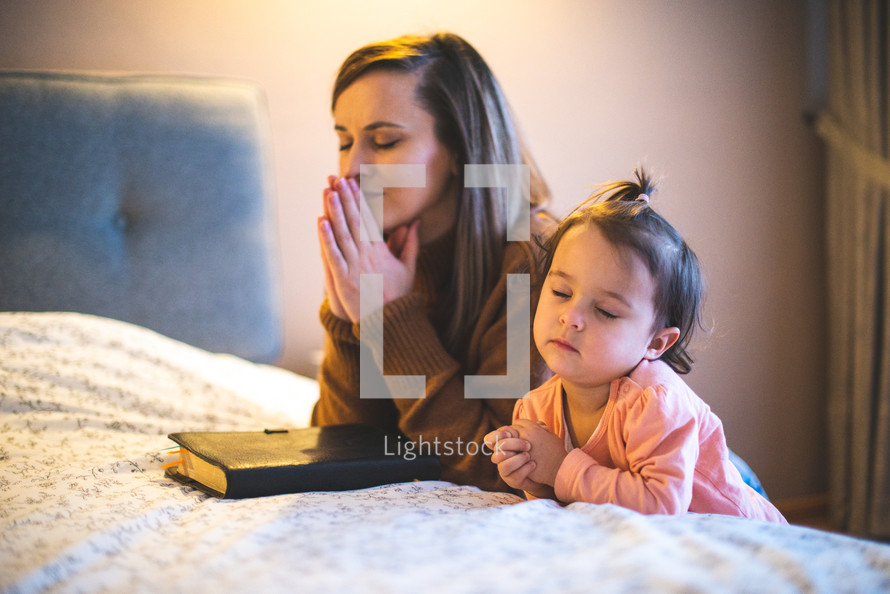 a mother and daughter praying bedside 