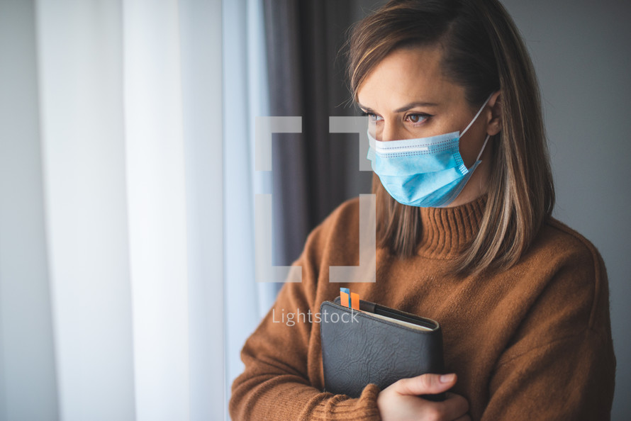 a woman in a face mask holding a Bible 