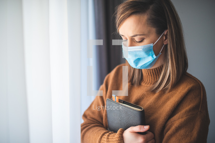 a woman in a face mask holding a Bible 