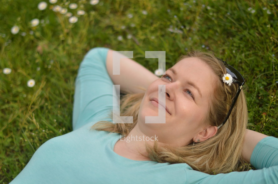 Young woman laying relaxed and daydreaming with open eyes in a meadow. 
