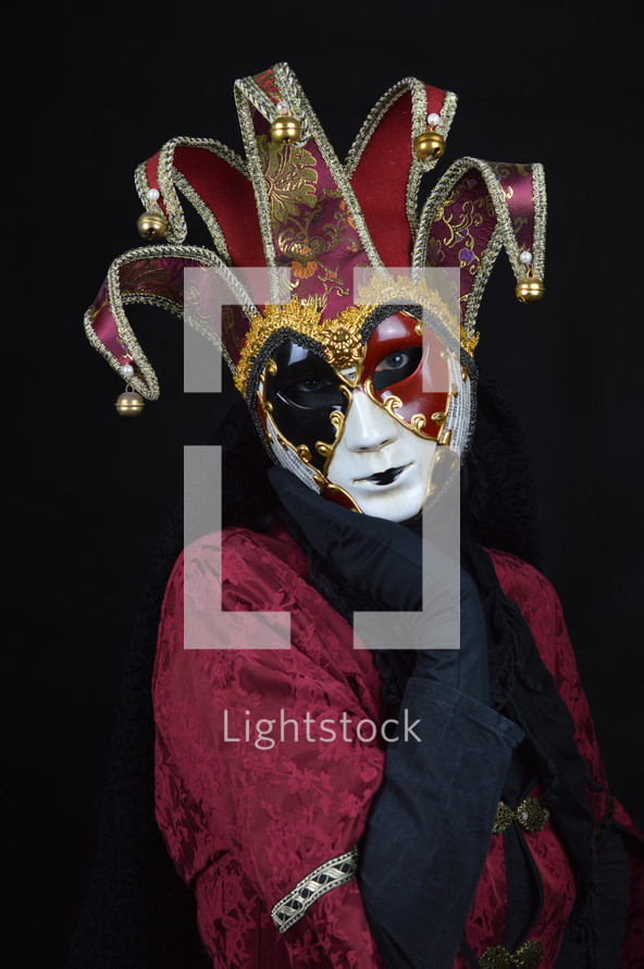 woman disguised with red white and black Venetian mask posing in front of neutral black background
