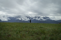 Man walking in the grass near snowy mountains