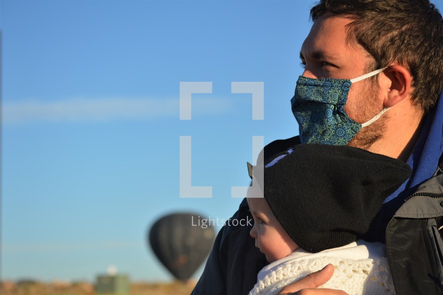 a father holding an infant and hot air balloons 