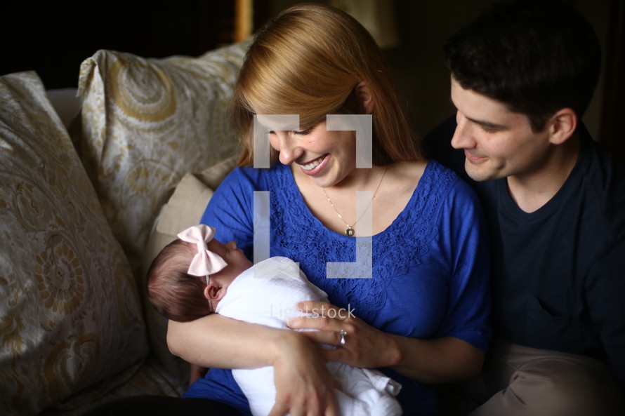 Smiling couple sitting on a sofa holding an infant.