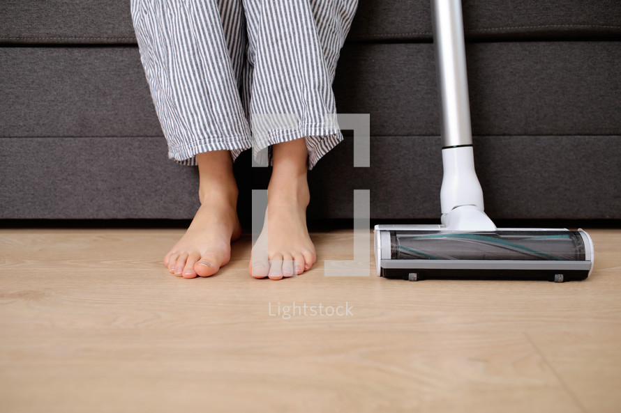 Young woman with vacuum cleaner sitting on sofa at home
