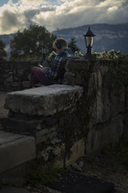 Man with headphones sitting next to stone wall 