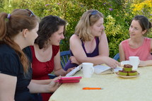 women's group reading scripture together sitting at a table in the garden for a Bible study