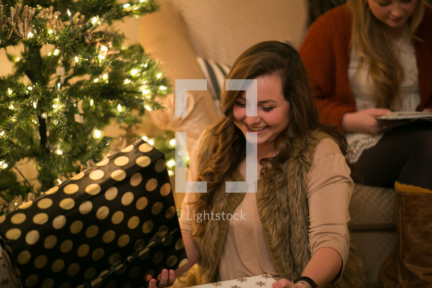 Two women sit near a Christmas tree and presents.