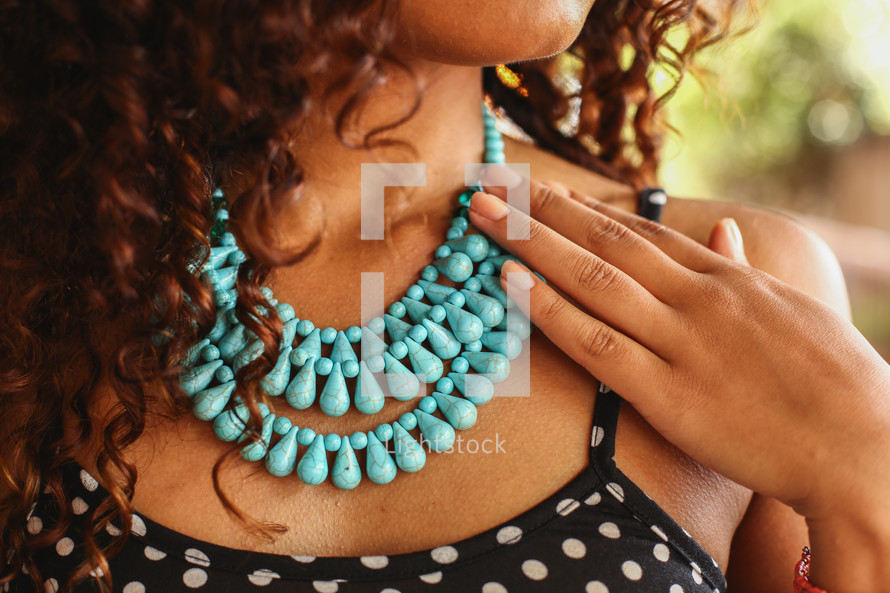 a woman touching her teal beaded necklace 