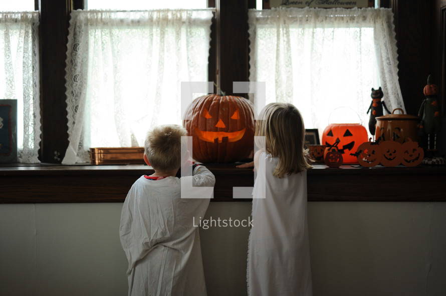 children in capes standing in front of a jack-o-lantern 