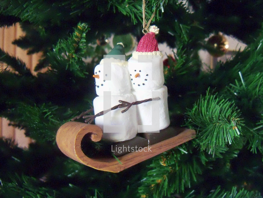 A couple of snowmen or snow people  sleigh riding on a sleigh Christmas ornament hanging on a Christmas tree showing an animated happy Christmas couple sleigh riding together. 