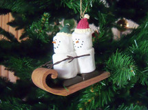 A couple of snowmen or snow people  sleigh riding on a sleigh Christmas ornament hanging on a Christmas tree showing an animated happy Christmas couple sleigh riding together. 