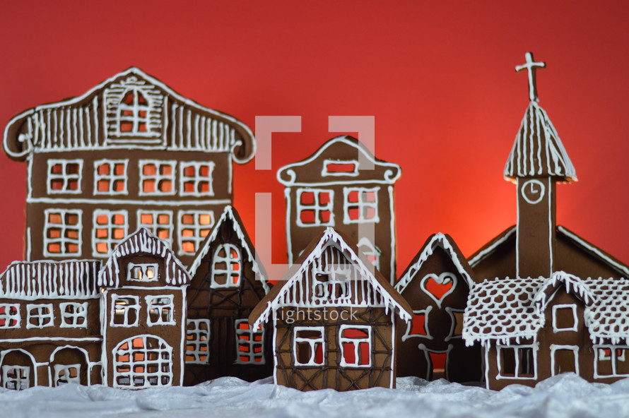 home made gingerbread village in front of red background on white snowlike velvet as advent decoration