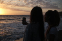 Young women with phone camera on the beach at sunrise
