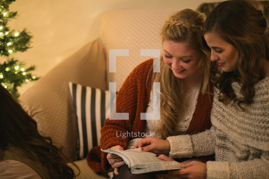 Two women reading the Bible together near a Christmas tree.