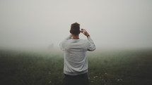 a man with a cellphone taking a picture of fog 