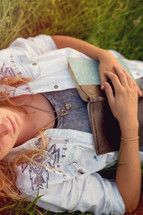 Woman laying in a field of grass holding a Bible.