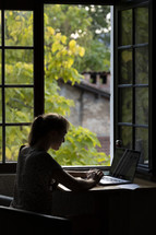 Woman looking at computer next to open window