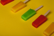 Brightly colored popsicles lined up on a yellow background.