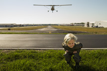 a boy child ducking as a plane flies over a runway