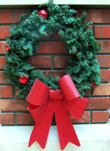 A  traditional old fashioned green evergreen Christmas wreath with a red bow ribbon against a brick hearth background reminding viewers that the Christmas season is here. 