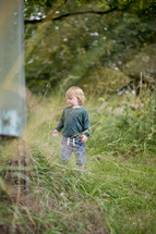 a toddler boy standing outdoors in tall grass 