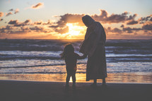 Jesus standing on a beach holding hands with a little girl 
