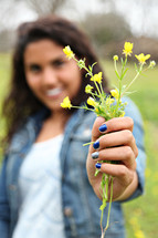 A woman holding a sprig of yellow wildflowers.