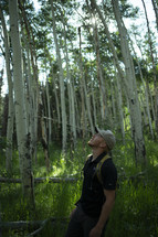 man looking up standing in a forest 