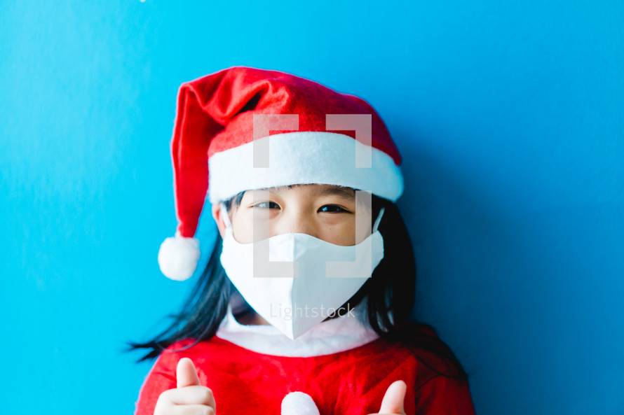 a little girl in a Santa Suit wearing a face mask 
