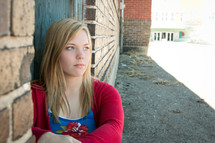 teen girl sitting against a wall outdoors 