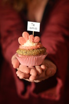 Woman offering a cupcake with pink hearts and a sign saying TE AMO.
