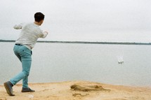 A young man throwing rocks in a lake.