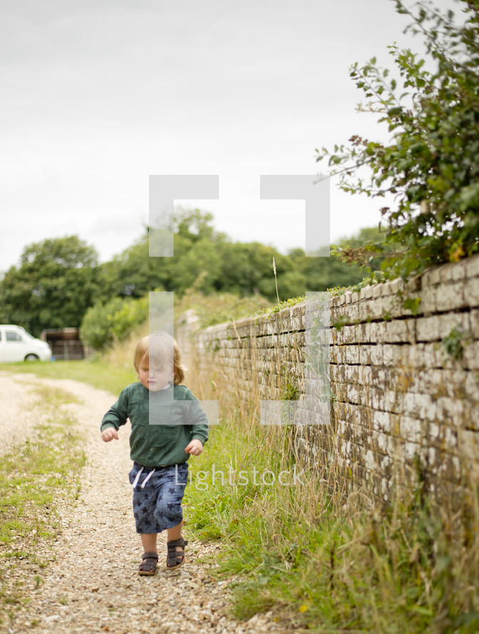 toddler boy running along a gravel path 