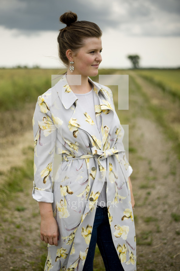 a woman in a trench coat standing in a plowed field 