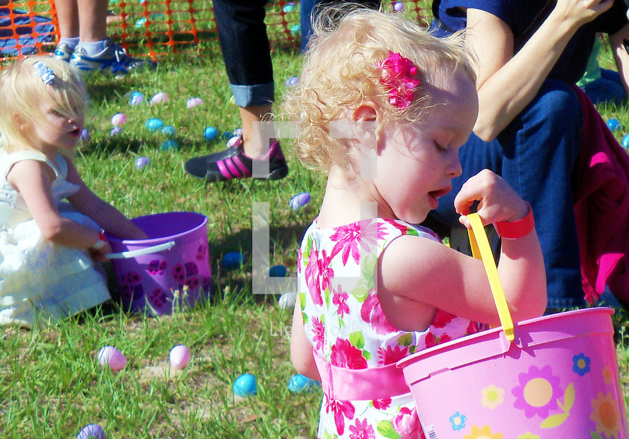 Two young sisters fill their baskets with Easter Eggs at a local outdoor church Easter Egg hunt for kids of all ages for Easter. 