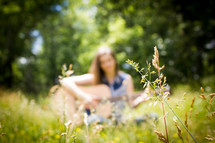 blurry image of a woman sitting in a field playing a guitar 