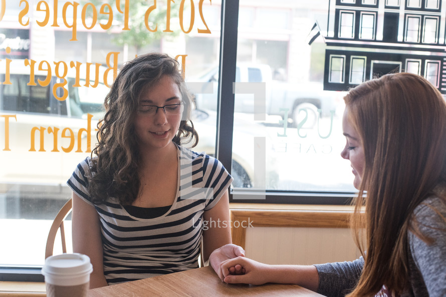 young women at a coffee shop for a Bible study praying 