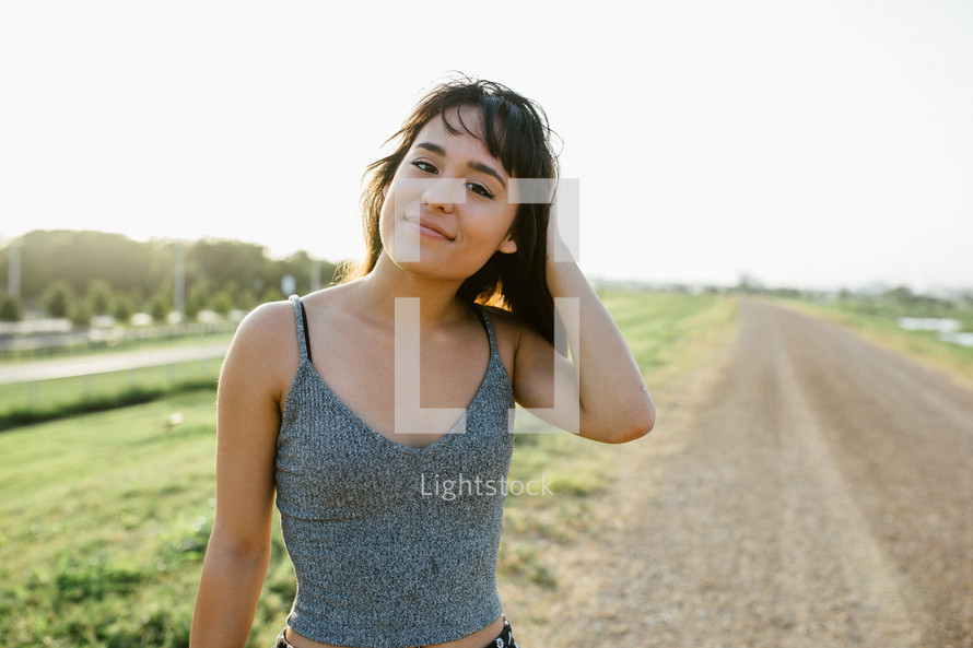 a young woman standing on a rural dirt road 