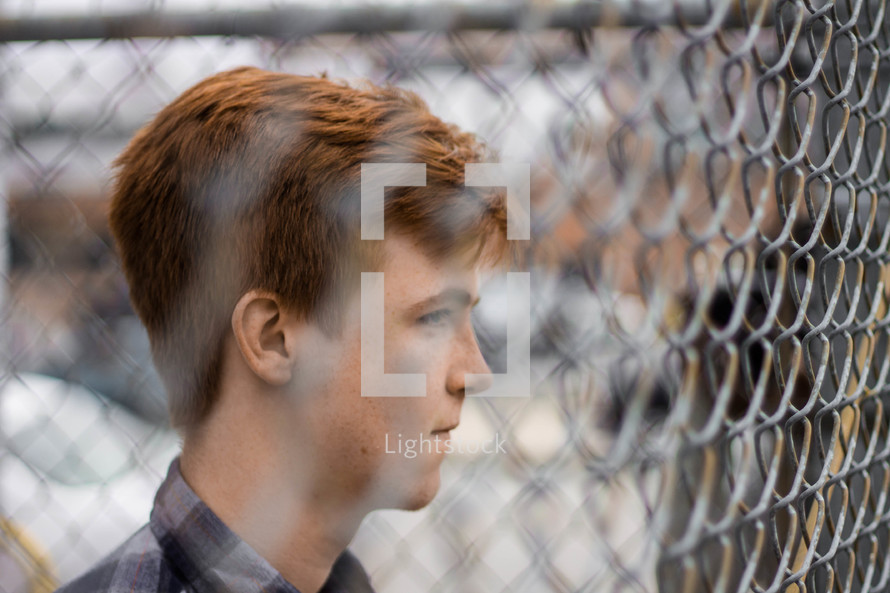 a young man standing in front of a chain link fence 