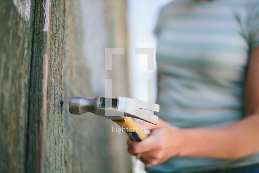 Hammer being held by a woman, hammering into a wooden wall