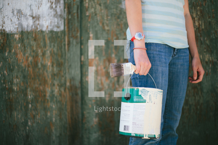 Woman holding a bucket of paint and paintbrush.