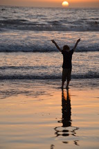 child with raised arms in adoration at the beach. 