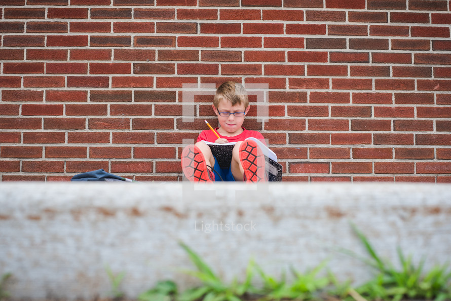 a boy doing his homework leaning against a school building 