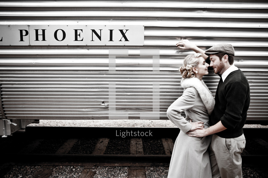 Couple, dressed in 1940's costumes, standing in front of an old train