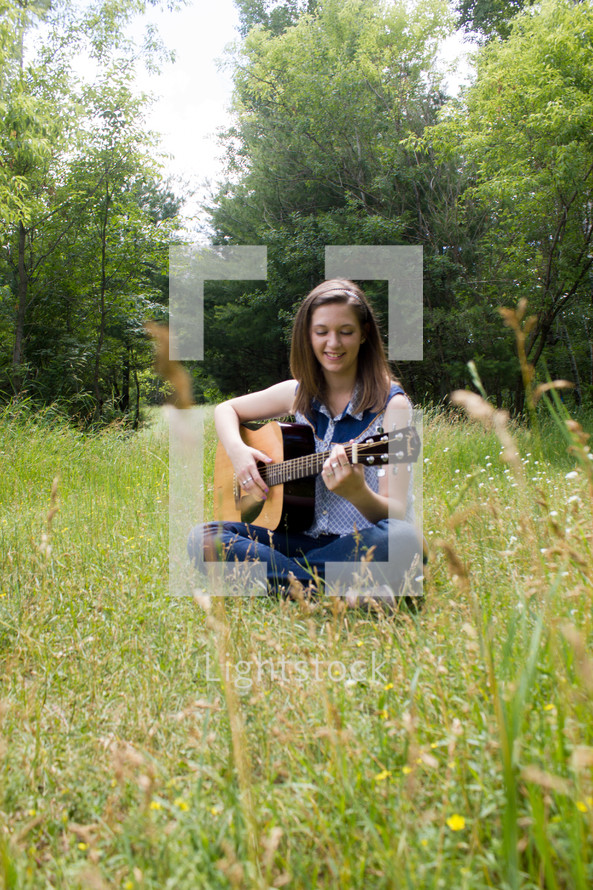 woman sitting in a field playing her guitar 