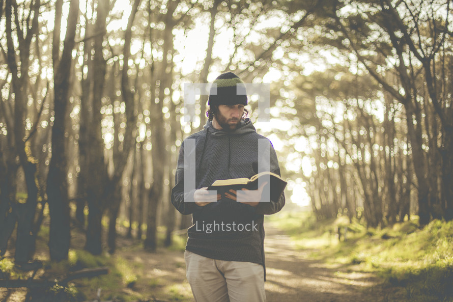a man standing in a forest reading a Bible 