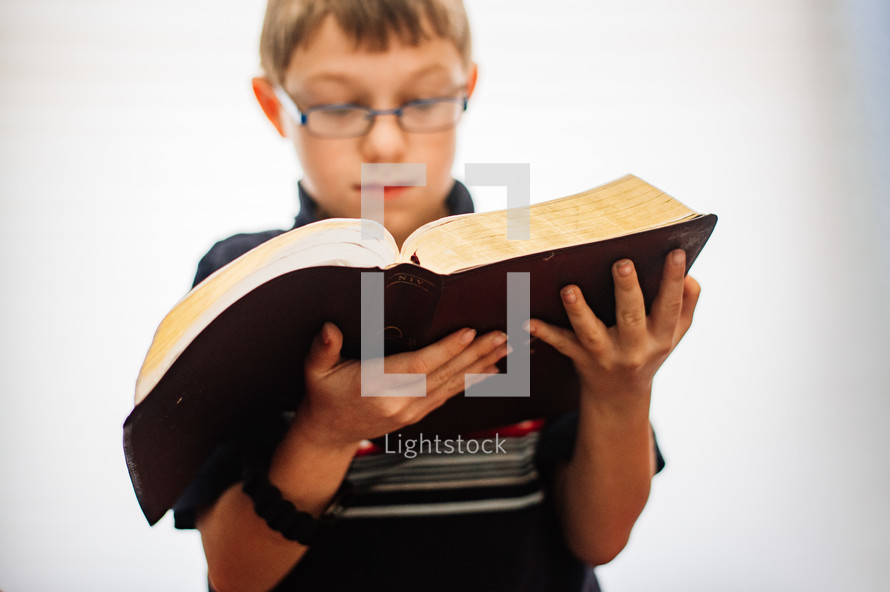 A 11 year old boy reading an open Bible  with a white background