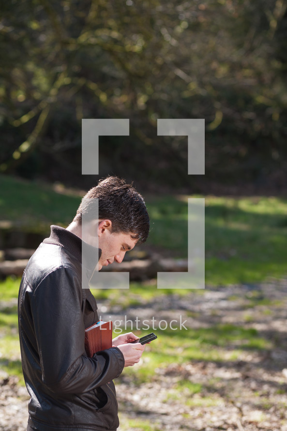 man holding a Bible and texting on his phone outdoors